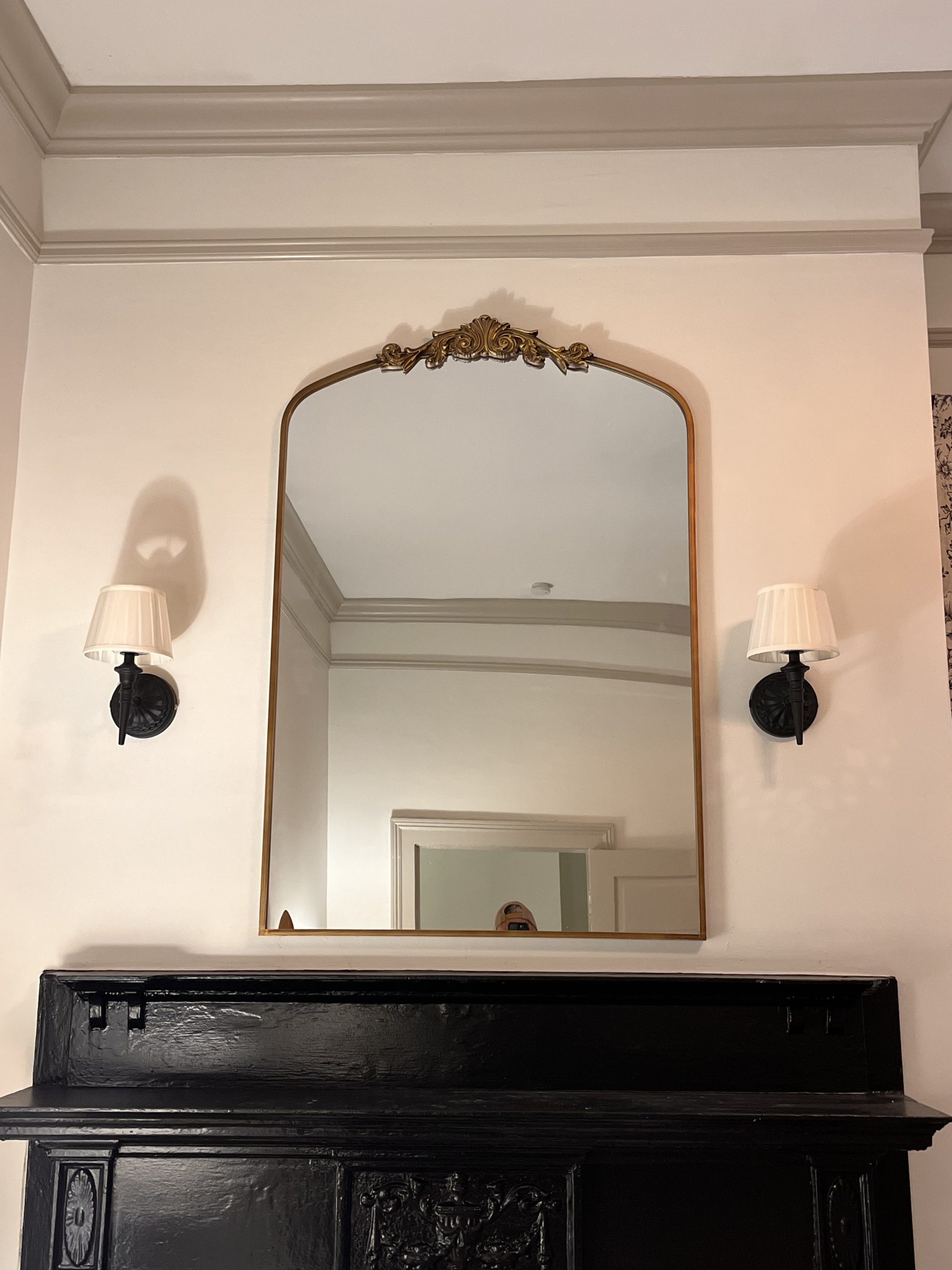 Arched gold mirror hung between two black wall sconces above a black mantel