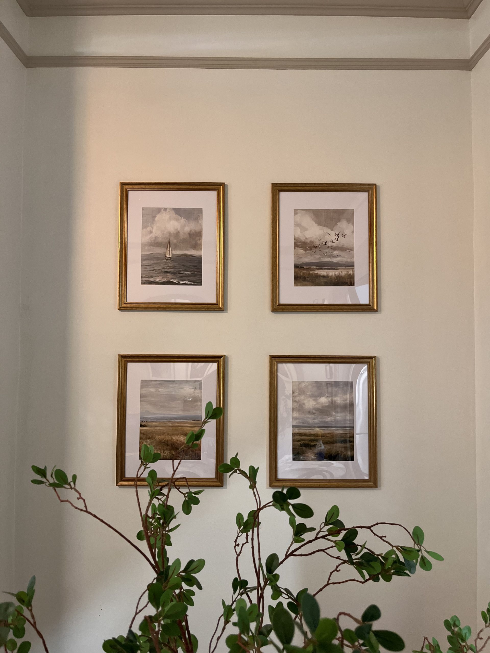 Four gold-framed coastal prints hung level in a grid on a wall