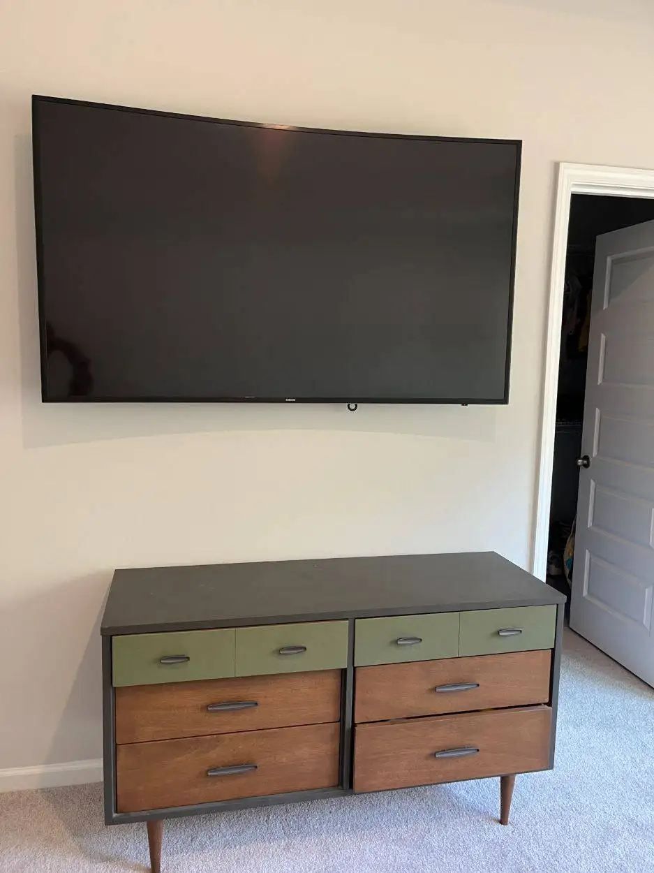 Curved Samsung TV mounted on a bedroom wall above a mid-century dresser