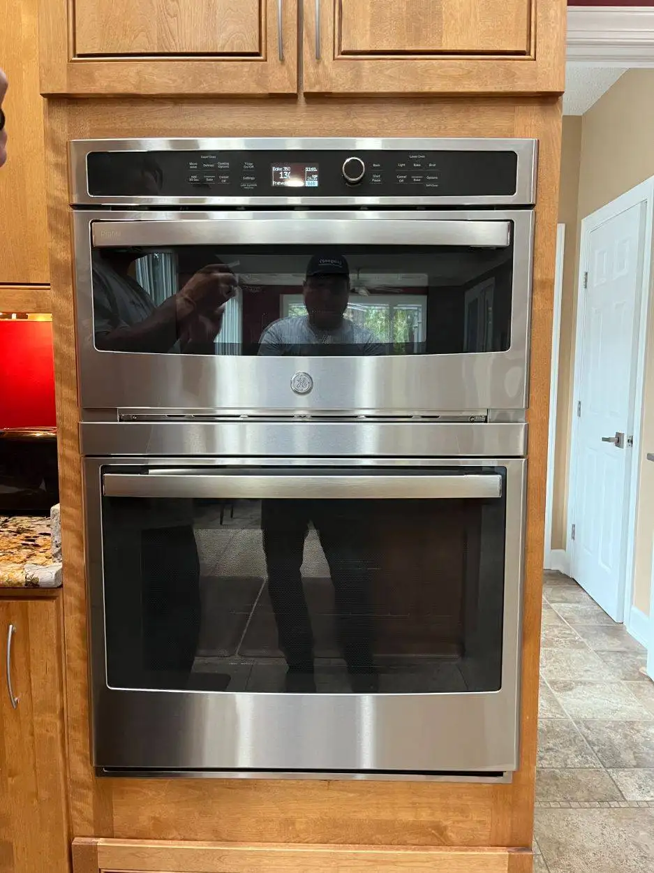 Installation of a stainless steel oven and microwave set within wood-finish kitchen cabinetry.