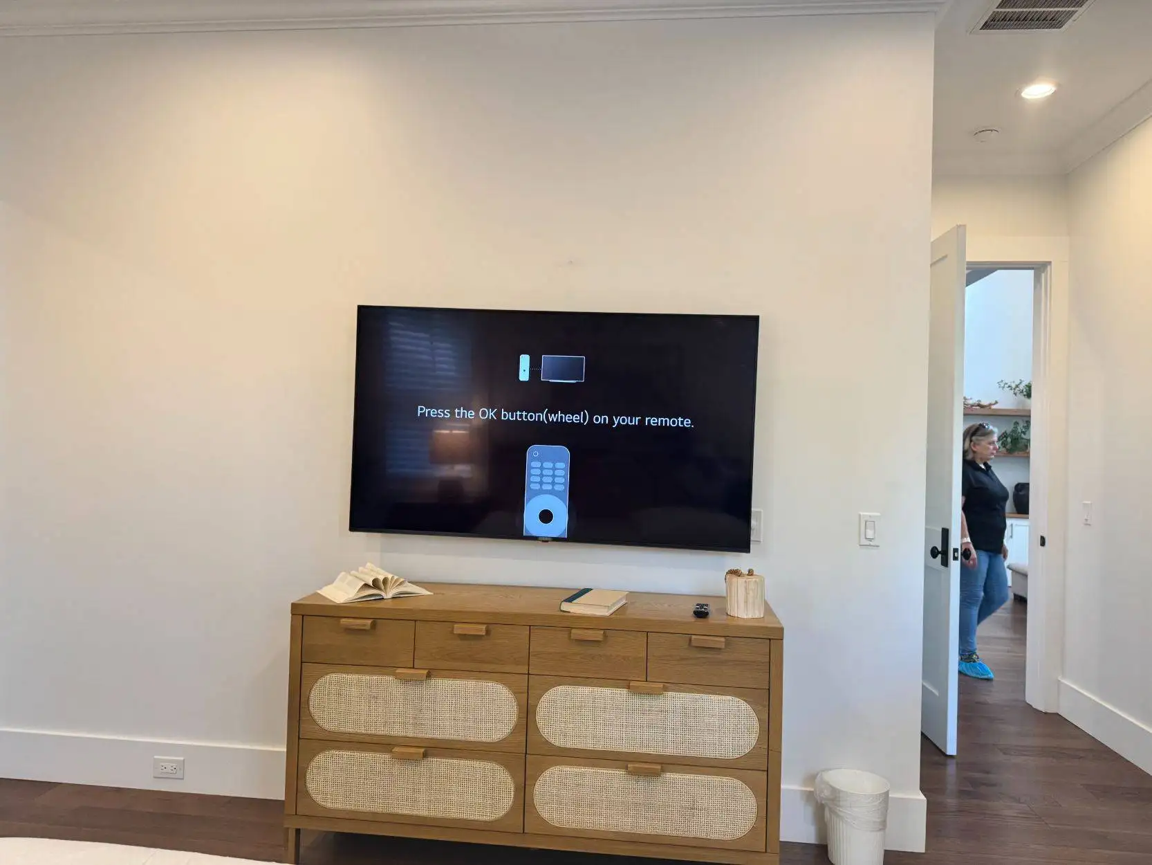 Large flat-screen TV mounted level on a bedroom wall above a rattan dresser